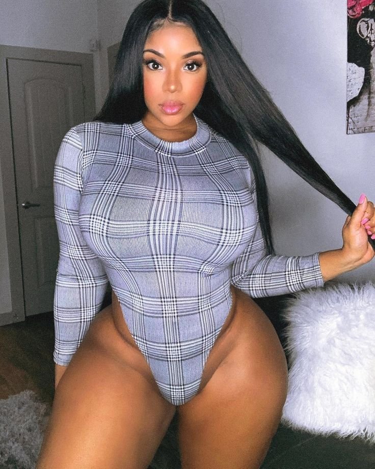 Confident curvy woman wearing a fitted plaid bodysuit indoors with sleek long hair