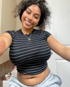 Playful curvy UK phone chat model Caleya Brighton smiling with natural curls and relaxed confident presence