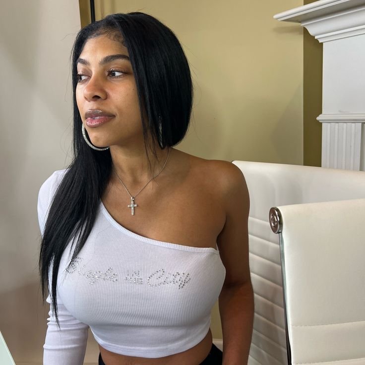 Woman wearing a white one-shoulder top seated indoors with a calm expression