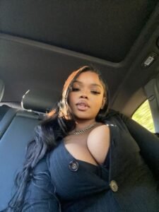 Confident curvy woman with long dark hair wearing a black outfit seated inside a car