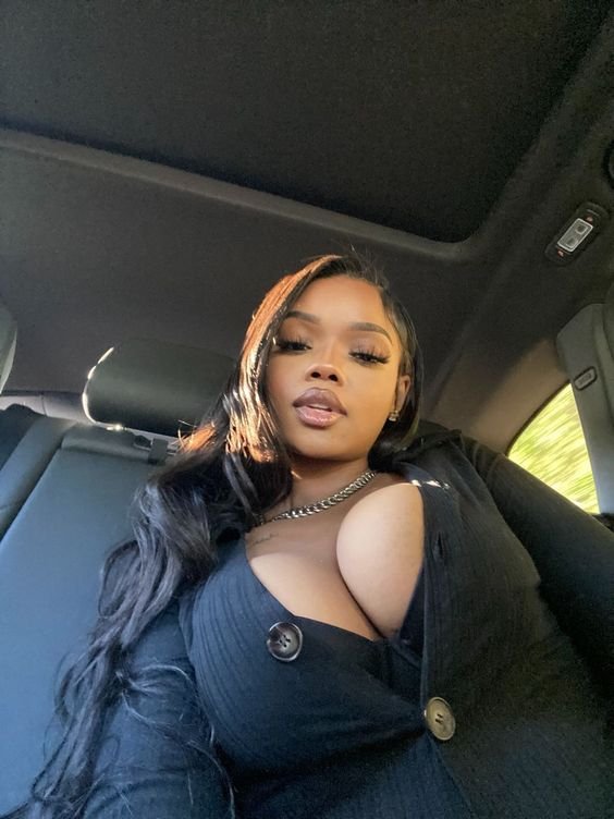 Confident curvy woman with long dark hair wearing a black outfit seated inside a car