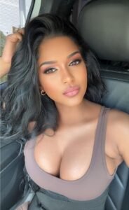 Confident woman with long wavy hair wearing a neutral sleeveless top seated in a car