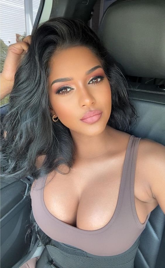 Confident woman with long wavy hair wearing a neutral sleeveless top seated in a car