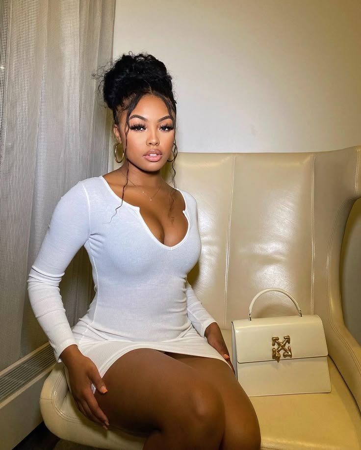 Curvy woman in a fitted white dress seated indoors with elegant, confident pose