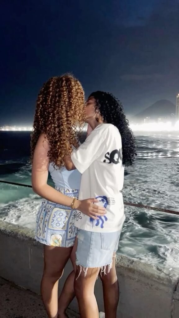Girls on girls chat UK profile featuring two women by the seaside Lesbian phone chat UK female duo with natural curly hair Women seeking women chat profile on a coastal walkway Girls on girls phone chat UK profile image Lesbian chat lines UK confident female pair Adult chat UK girls on girls category profile