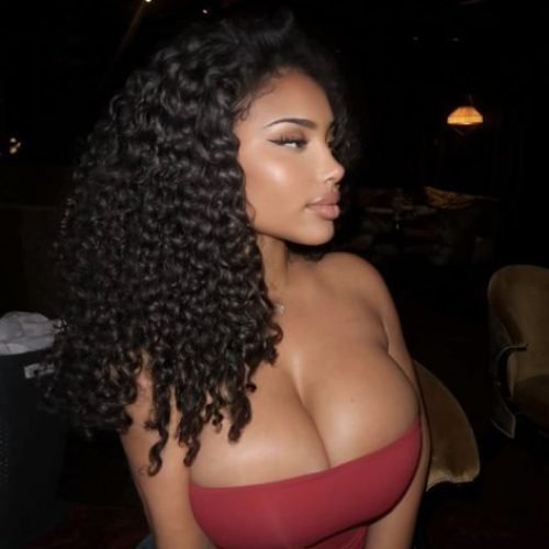 Woman with long curly hair wearing a strapless red dress indoors at night