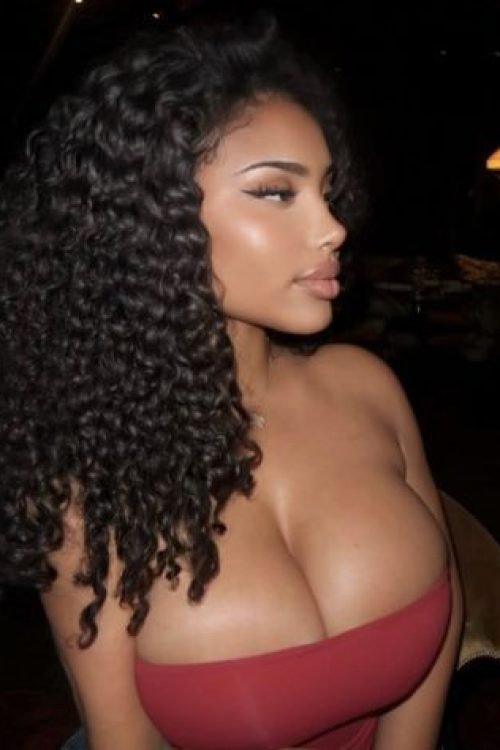 Woman with long curly hair wearing a strapless red dress indoors at night