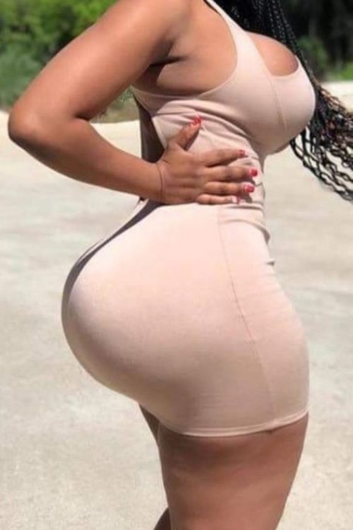 Curvy woman wearing a fitted beige dress standing confidently outdoors with natural pose