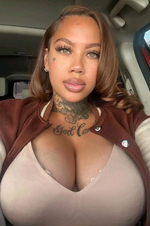 Confident curvy UK phone chat model Ravina Lux with tattoos and soft glam makeup