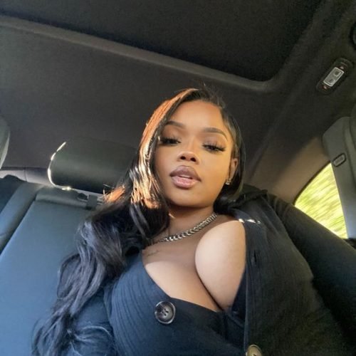 Confident curvy woman with long dark hair wearing a black outfit seated inside a car