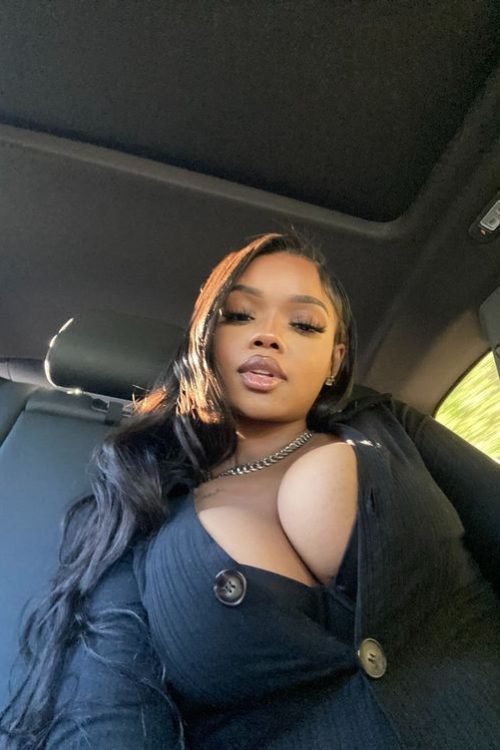Confident curvy woman with long dark hair wearing a black outfit seated inside a car