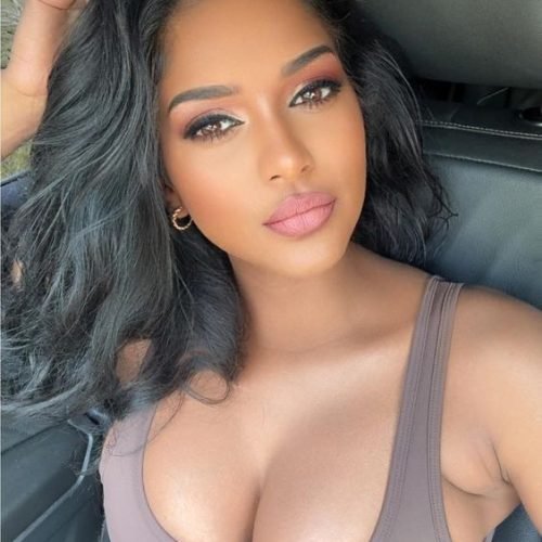 Confident woman with long wavy hair wearing a neutral sleeveless top seated in a car