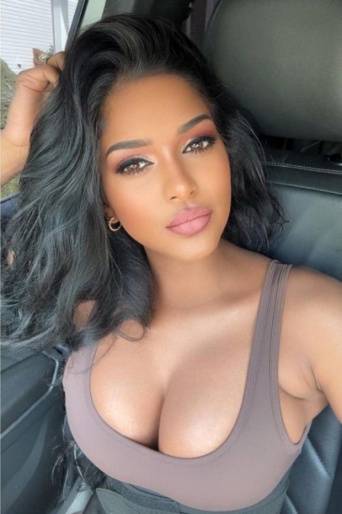 Confident woman with long wavy hair wearing a neutral sleeveless top seated in a car