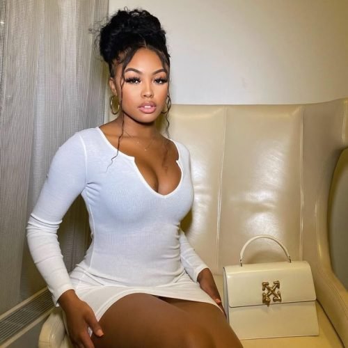 Curvy woman in a fitted white dress seated indoors with elegant, confident pose