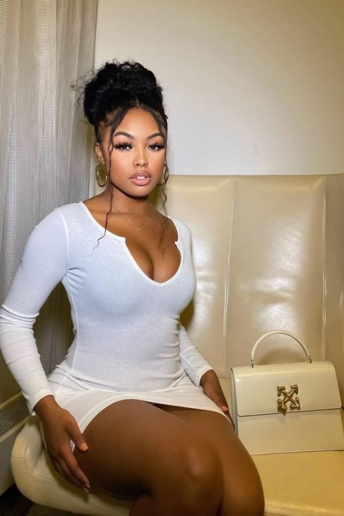 Curvy woman in a fitted white dress seated indoors with elegant, confident pose